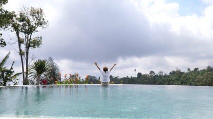 Woman jumps out of a swimming pool and splashes water in appreciation of life. Palm trees in the background