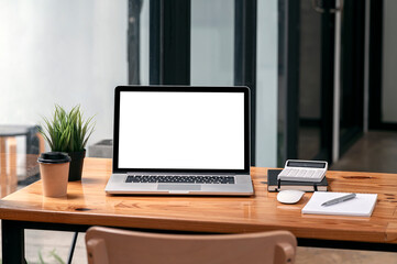 Mockup blank screen laptop computer and supplies on wooden table in modern office room.