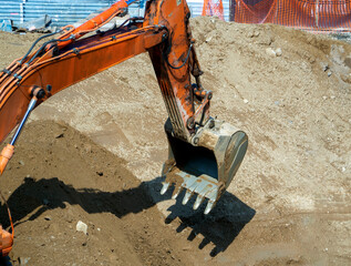 Fototapeta premium The excavator bucket is lowered into the pit to pick up the soil from there. Close-up. Background with a construction site for industry and business.