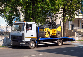 Fototapeta na wymiar A tow truck transports the road roller on a stationary platform to the place of work. Background for business and industry.