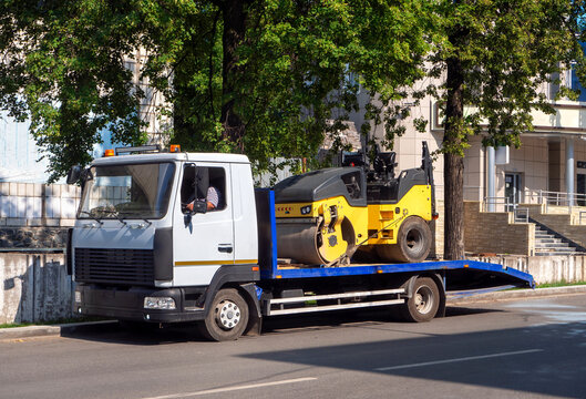 A tow truck transports the road roller on a stationary platform to the place of work. Background for business and industry.