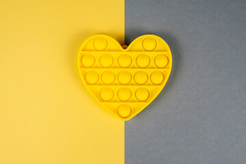 Yellow heart pop-it toy isolated on a background in trendy colors. Color of 2021. Yellow, grey isolate.
