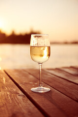 White wine in a champagne glass on a sunset. Sparkling cold champagne on a wooden pier. Single drink with warm light. Relax concept photo. Vertical photo.