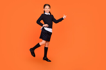 Fototapeta na wymiar Full length body size view of attractive glad cheerful preteen girl demonstrating copy space isolated over bright orange color background