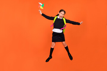 Fototapeta na wymiar Photo of energetic schoolgirl jump hold propeller toy wear uniform rucksack isolated orange color background