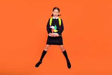 Full length photo of small girl jump amazed hold pinwheel wear glasses bag long socks formalwear isolated on orange color background