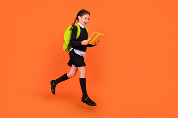Fototapeta na wymiar Full length body size view of pretty cheerful schoolgirl jumping reading diary isolated over bright orange color background