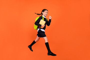 Fototapeta na wymiar Profile photo of active schoolgirl jump hold book run wear uniform backpack isolated orange color background