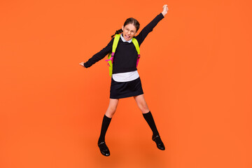 Full length body size view of pretty lucky cheerful schoolgirl jumping rejoicing having fun isolated over bright orange color background