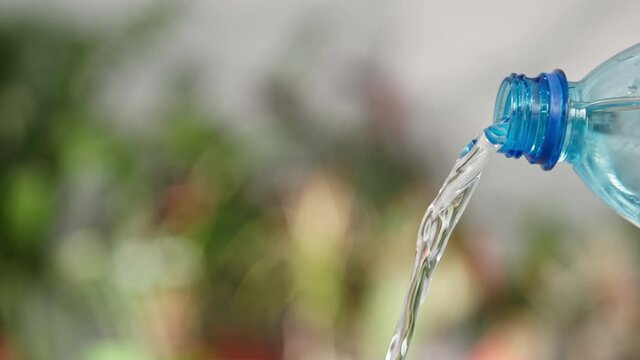 clean cool water is pouring a plastic with a transparent blue bottle on a green background, close-up