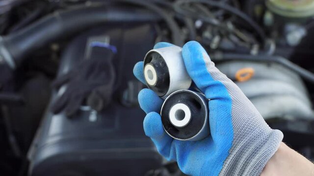 master in glove holds lever silent block in his hand against background of engine. rubber metal hinge, elastic part is connected to internal and external connections by vulcanization. car service.