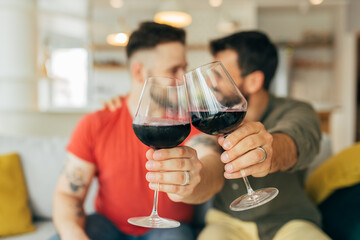 Close up of gay married couple toasting with red wine at home. They are celebrating love.