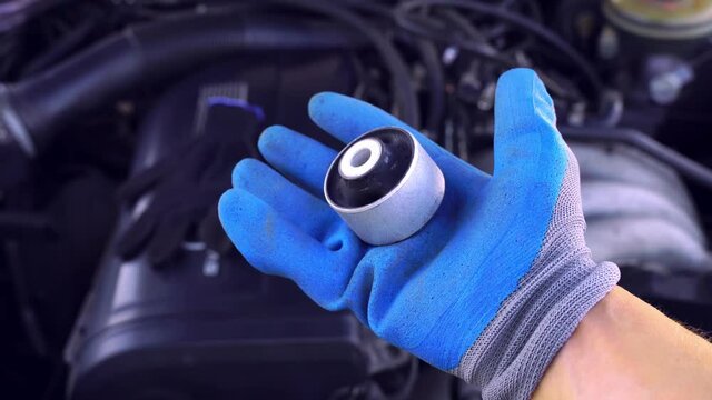 master in glove holds lever silent block in his hand against background of engine. rubber metal hinge, elastic part is connected to internal and external connections by vulcanization. car service.