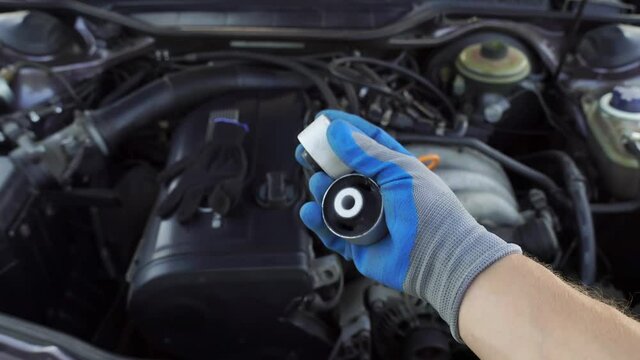 master in glove holds lever silent block in his hand against background of engine. rubber metal hinge, elastic part is connected to internal and external connections by vulcanization. car service.