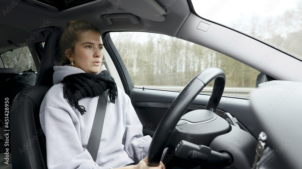 Wall mural Young woman with natural look driving a passenger car on a German highway. The young woman shows various emotional reactions to the traffic event.