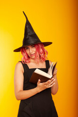 Evil female wizard holding a magic broom. Indoor photo of a wicked woman in a witch costume posing in halloween with a book of spells in her hands.