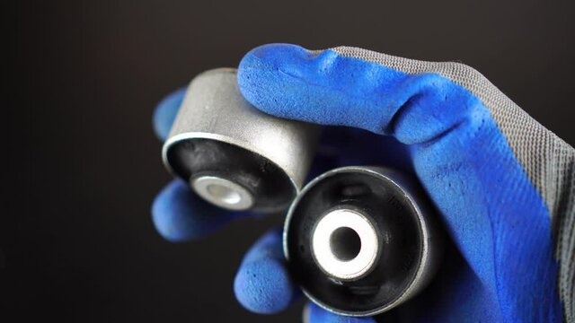 a gloved master holds a silent block lever in his hand on a black background. rubber metal joint, the elastic part is connected to the internal and external joints by vulcanization. car service.
