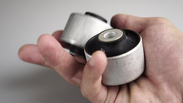 a gloved master holds a silent block lever in his hand on a white, background. rubber metal joint, the elastic part is connected to the internal and external joints by vulcanization. car service.
