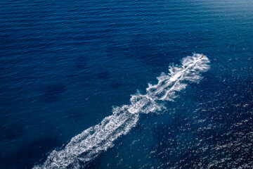 Aerial view of a sports jetski cruising over blue sea and leaving a trail of white bubbles behind