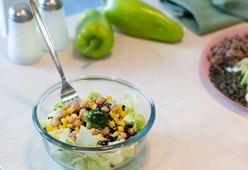 Fresh Salad in bowl. Chickpea with boiled corn, broccoli, lettuce, sesame. In the background is a plate with pumpkin seeds, green peppers and salt cellar. Healthy lifestyle concept