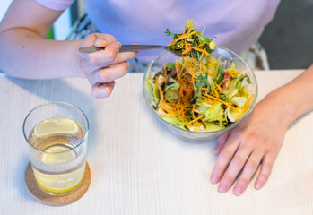 Healthy eating, dieting and people concept - close up of young woman eating vegetable mixed salad in restaurant, in dining table. Dieting concept. Water with lemon and salt on the table