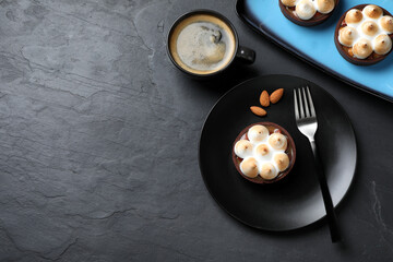 Delicious salted caramel chocolate tarts with meringue and coffee served on black table, flat lay. Space for text