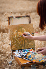 Close-up shot of a painting of three ears of rye on easel. Professional artist working on beautiful still life painting