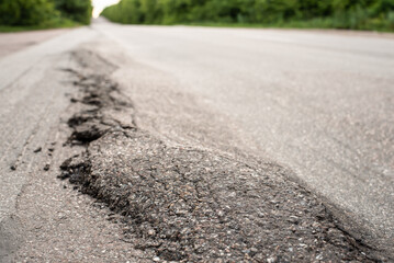 Close-up photo of damaged road in the countryside. Asphalt surface crushed and ran down due to heavy trucks driving. Problem of overloaded trucks