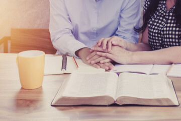 Close up of two woman hands pray together with the holy bible on wooden table, bible study and pray...
