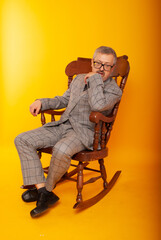 senior elderly American, European sitting relaxed in a rocking chair against a yellow background.

low-key portrait of man sitting in wooden rocking chair isolated on yellow