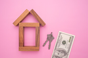 Small wooden house with house keys and US dollars banknote isolated on pink background for home loans concept