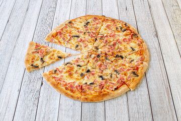 Whimsical family pizza sliced with melted mozzarella cheese, lots of ham slices and mushrooms on a white table