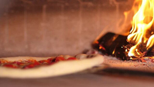 Baking pizza in the oven in pizzeria near open fire of burning wood