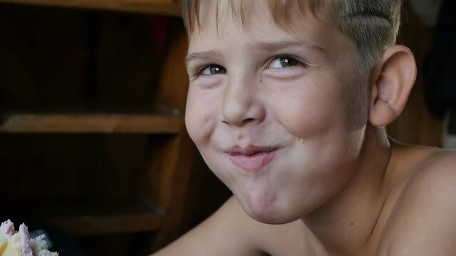 Portrait. Caucasian boy teenager with brown eyes with a naked body eats a sandwich early in the morning, smiles and looks into the frame. Close-up, slow motion