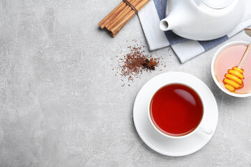 Obraz na płótnie Canvas Freshly brewed rooibos tea, scattered dry leaves, honey and spices on grey table, flat lay. Space for text