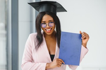 Beautiful young Afro American graduate in academic dress is holding diploma