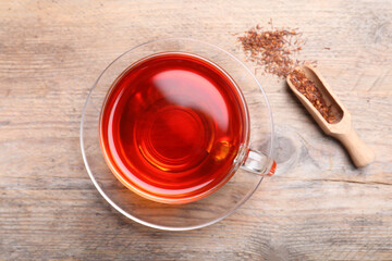 Freshly brewed rooibos tea and dry leaves on wooden table, flat lay