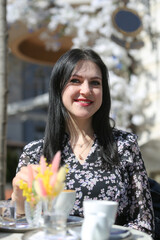 Smiling stylish woman in black shirt sitting at the table drinking coffee in the terrace of restaurant.