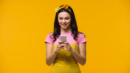 Young woman smiling while using smartphone isolated on yellow.