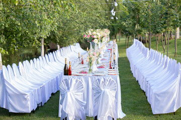 Wedding white table decoration and floral design positioned in a green garden