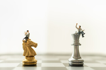 Business, Game and Planning Concept. Two businessman miniature figure people sitting and reading neewspaper on knight and king chess pieces on chessboard.