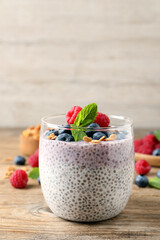 Delicious chia pudding with berries, granola and mint on wooden table, space for text