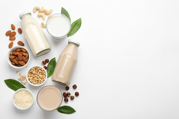 Different vegan milks and ingredients on white background, flat lay. Space for text