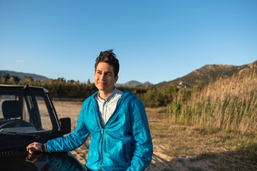Portrait of young caucasian man lying on car with country and rural background.
