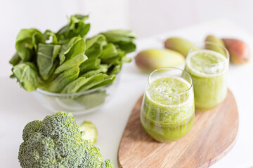 Fresh ingredients for healthy detox cocktail green color. Two glasses with beverage for diet on wooden plate, next lying broccoli and other vegetables and fruits.