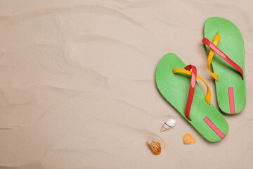 Pair of green flip flops and sea shells on sand, flat lay. Space for text