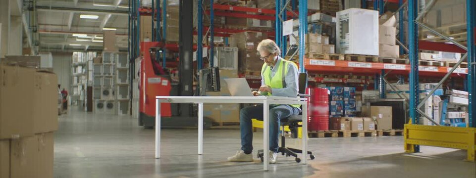 Warehouse worker or manager working on his laptop computer while sitting at a desk.