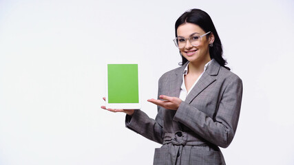 Businesswoman smiling while pointing at digital tablet with green screen isolated on white.