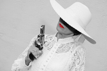 black and white portrait of a woman in a white hat and red lipstick with a revolver in her hands