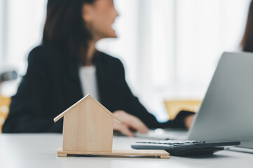 businessman analyzing data on laptop with a business woman using a calculator at the office. Model houses and banknotes.